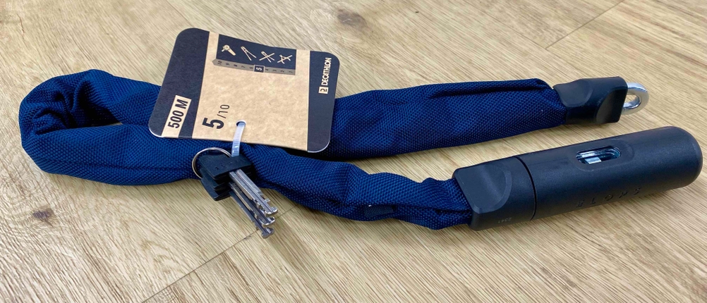 Auf einer Holzfläche liegt ein geöffnetes Kettenschloss mit Label und Schlüsseln.