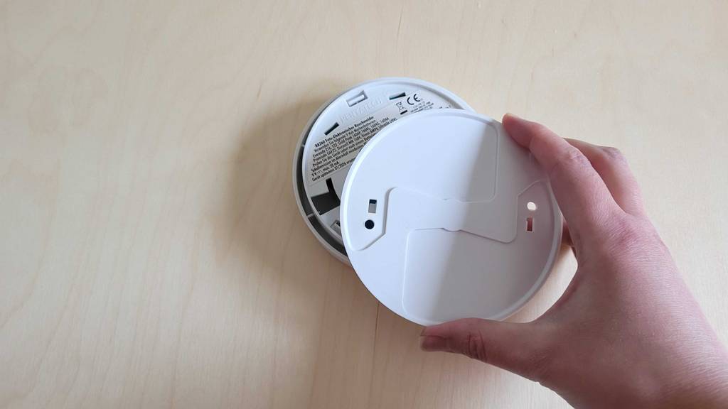 Eine Hand hält die Wandbefestigung über einen Elro-Rauchmelder im Test.