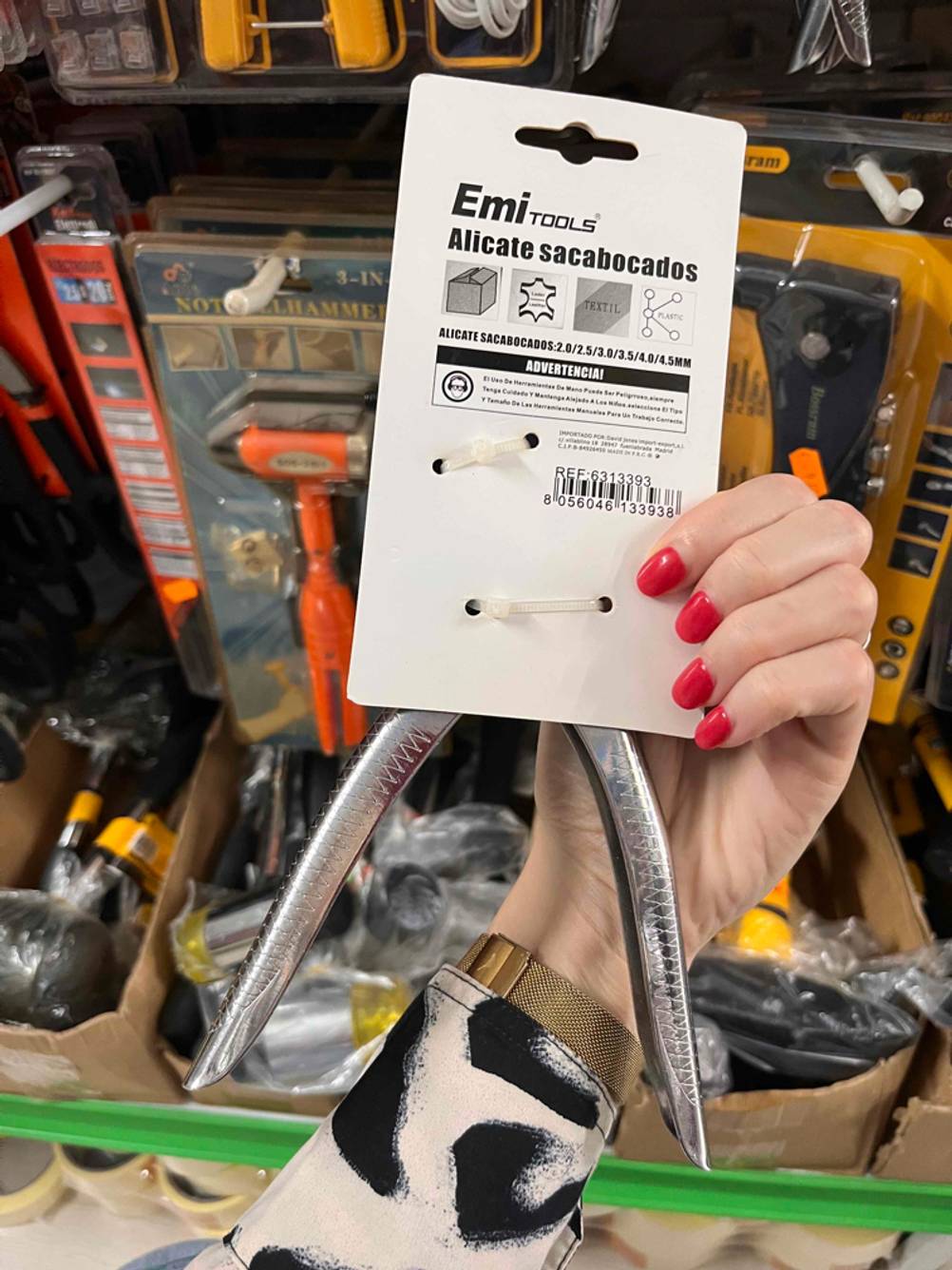 Getestet: Eine Hand hält die Rückseite einer verpackten Revolverlochzange vor ein Regal.