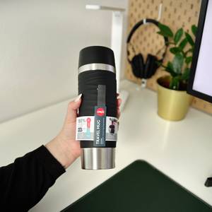 Der Thermobecher Waves Grande von Emsa wird von einer Frau an einem Schreibtisch hochgehalten.