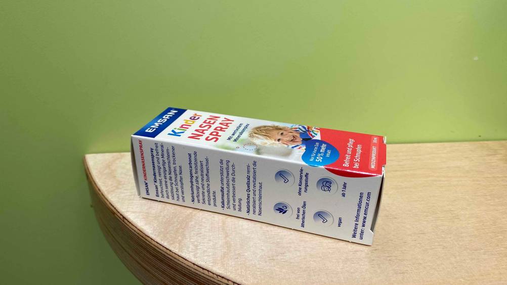 Die Eigenschaften eines getesteten Nasensprays für Kinder stehen auf der Seite einer auf Holzfläche liegenden Verpackung.