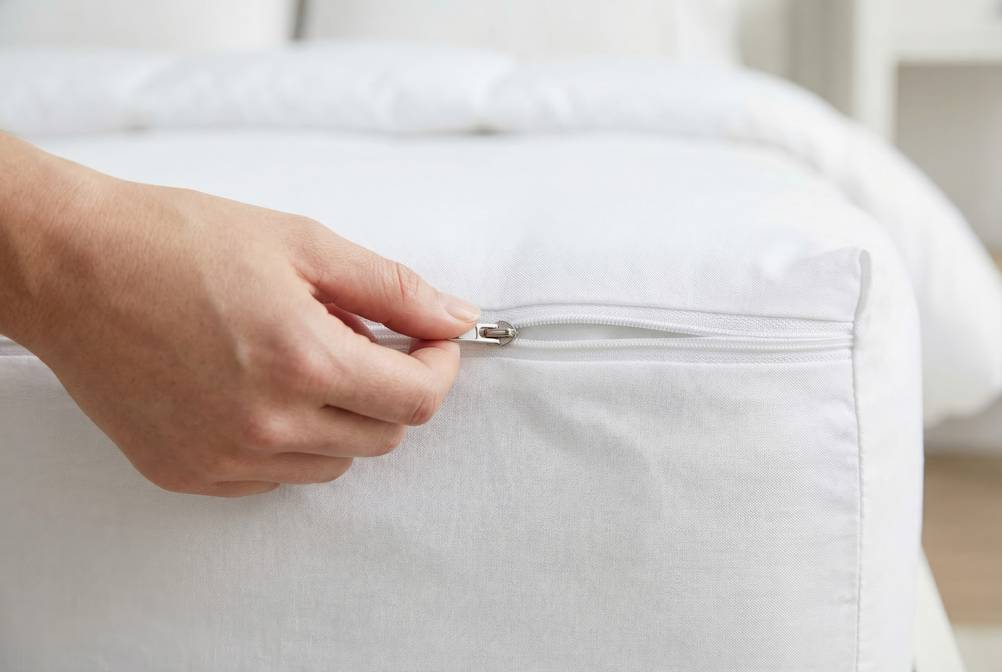 Encasing-Test: Eine Frau öffnet den Reißverschluss eines Matratzenschutzes.