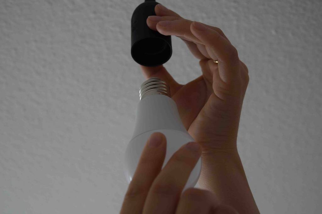 Eine Hand schraubt eine getestete Energiesparlampe in eine Fassung.