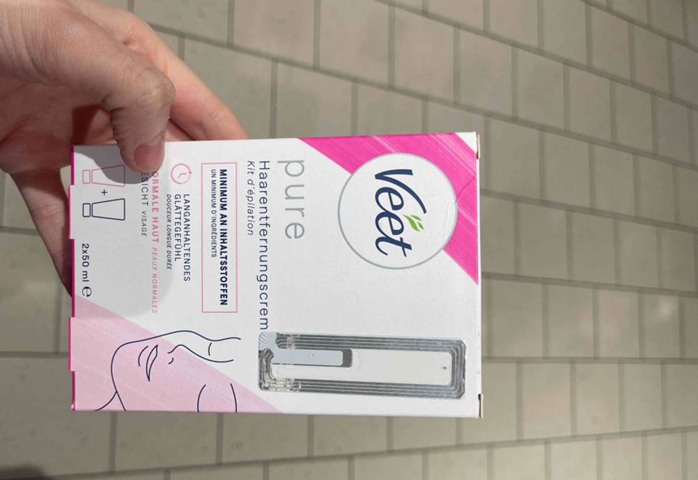 Eine Hand hält eine Packung Enthaarungsmittel zum testen.
