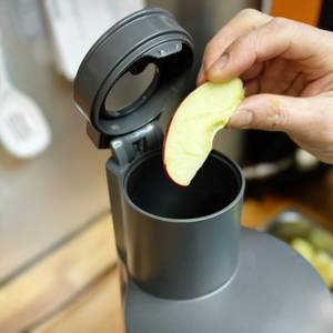 Eine Hand hält ein Apfelstück und legt es in den Einfüllschacht des Kenwood PureJuice Pro Entsafters. Der geöffnete Deckel zeigt den doppelten Einfüllmechanismus.