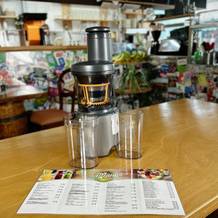 Der Kenwood PureJuice Pro Entsafter steht auf einem Holztisch mit einem Saftbehälter und dem Auffangbehälter. Im Hintergrund ist eine bunte Café-Umgebung zu sehen.