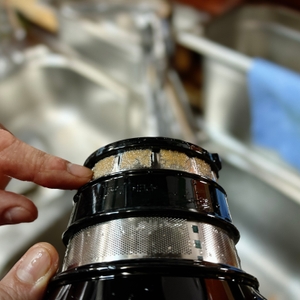 Eine Hand zeigt auf Fruchtreste, die sich im feinen Sieb des Kenwood PureJuice Pro Entsafters abgesetzt haben. Im Hintergrund ist eine Spüle zu sehen.