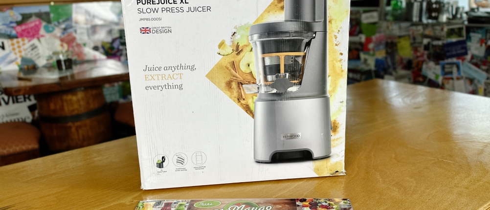 Die Verpackung des Kenwood PureJuice Pro Entsafters steht auf einem Tisch in einem Café. Ein Menü liegt davor.