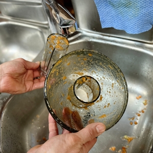 Der Deckel und der Saftbehälter des Philips HR1832/00 werden unter fließendem Wasser im Spülbecken gereinigt. Karottenreste sind noch sichtbar.