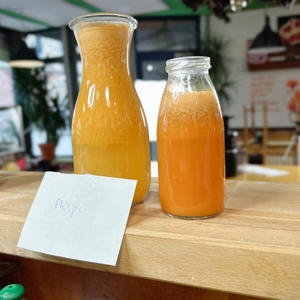 Zwei Glasflaschen mit frisch gepresstem Saft aus dem Philips HR1832/00 stehen auf einer Theke. Vor ihnen liegt ein handgeschriebener Zettel mit der Aufschrift 