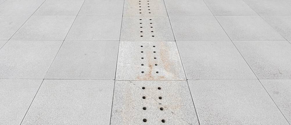 Entwässerungsrinne aus Beton mit kleinen Abflusslöchern in einem Gehweg getestet.