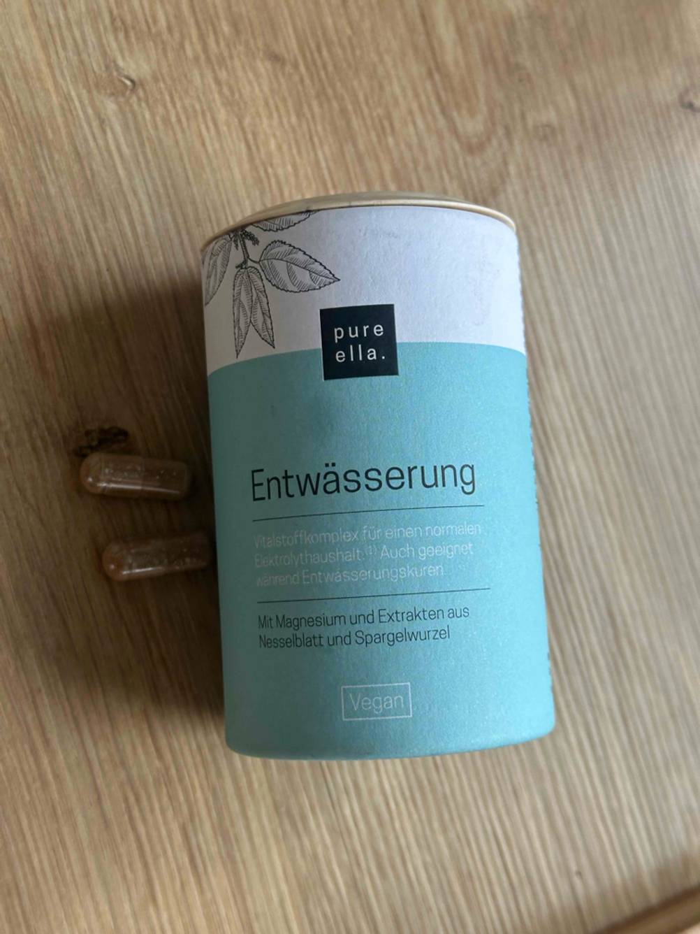 Eine Packung der Entwässerungstabletten im Test auf einem Holztisch liegend, zwei Kapseln daneben.