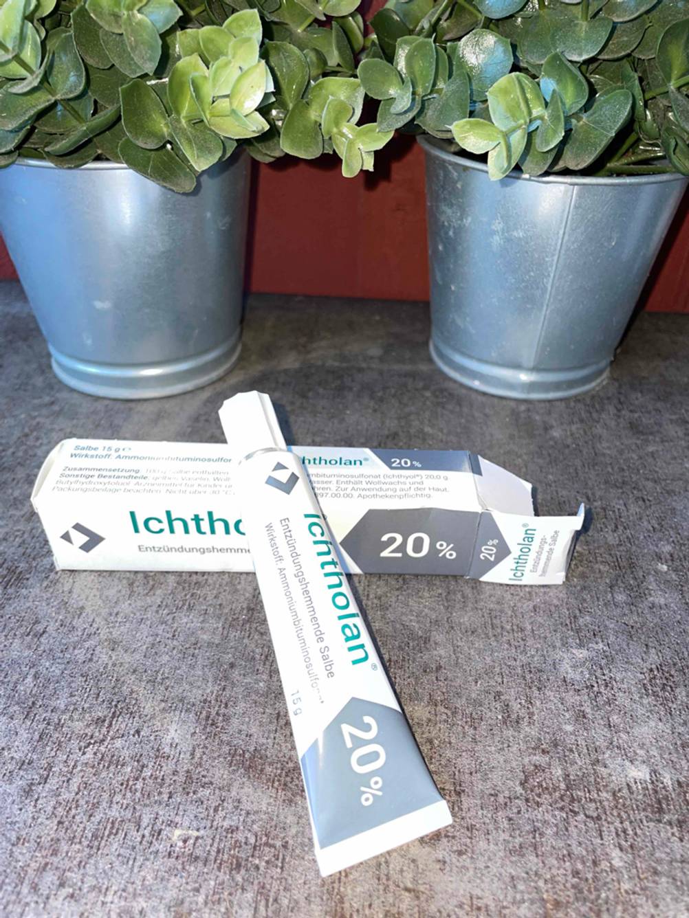 Entzündungshemmende Salbe getestet: Eine Tube liegt auf der Originalverpackung vor Pflanzentöpfen.