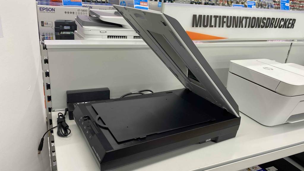 Ein Flachbettscanner im Test mit geöffnetem Deckel steht auf weißem Regal, von der Seite betrachtet.