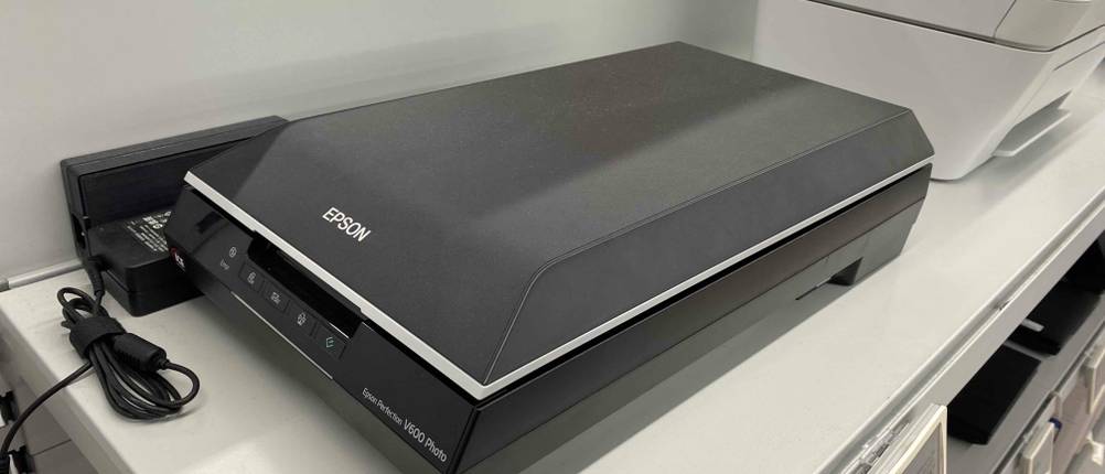 Ein getesteter Epson Flachbettscanner, von schräg vorn betrachtet, steht auf weißem Regal.
