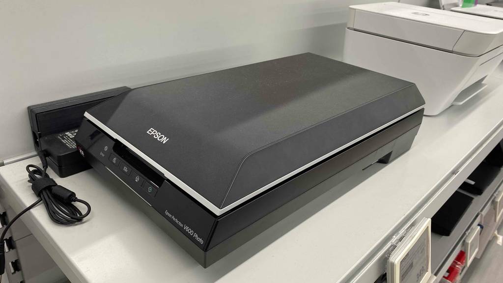 Ein getesteter Epson Flachbettscanner, von schräg vorn betrachtet, steht auf weißem Regal.