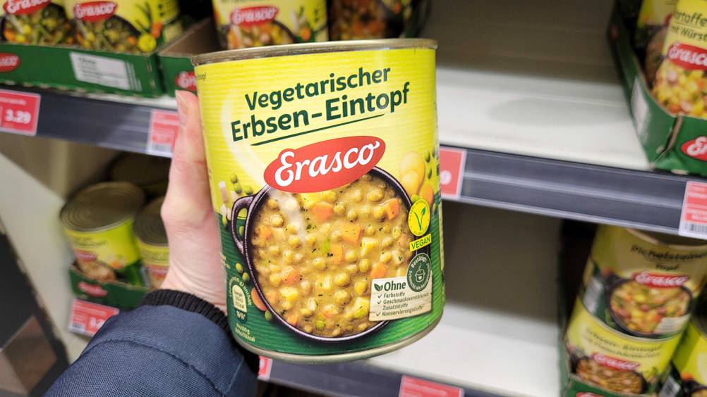 Eine Hand hält eine Dose des Erasco-Eintopfs im Test vor ein Regal.