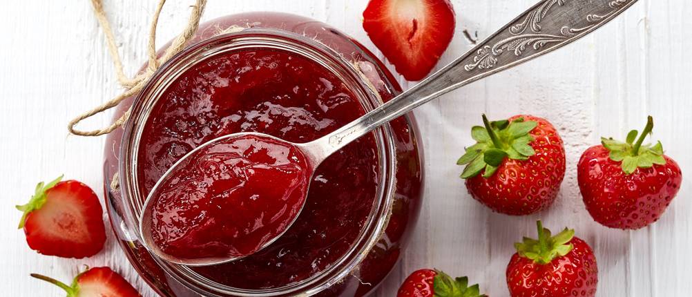 Erdbeermarmelade in einem Glas mit Löffel mit Erdbeeren daneben