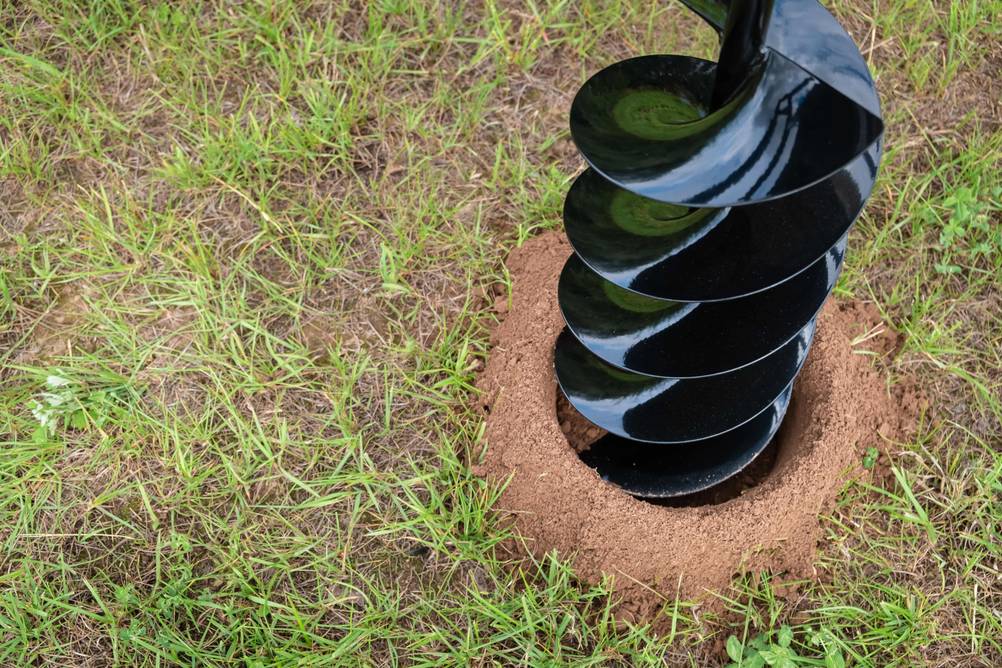 Erdbohrer im Test: eine schwarzlackierte völlig neu wirkende Schraube eines Erdbohrer steckt in einem Erdloch