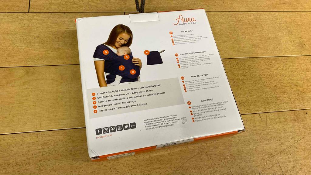 Rückseite der Originalverpackung eines getesteten Tragetuchs, die auf einem Holzboden liegt.