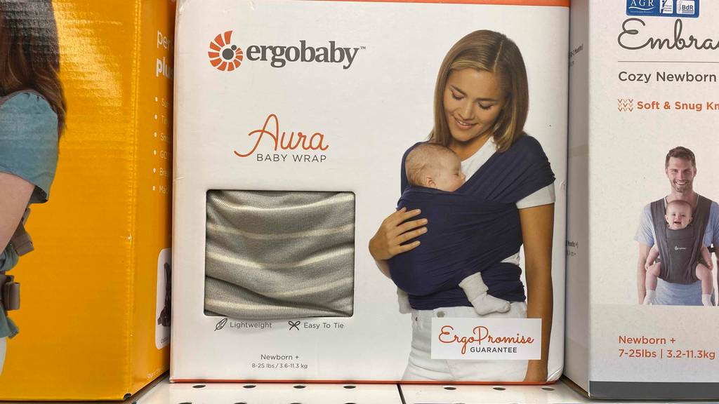 Tragetuch im Test: Frontansicht von verpackten Ergobaby Varianten in einem Regal neben anderen.