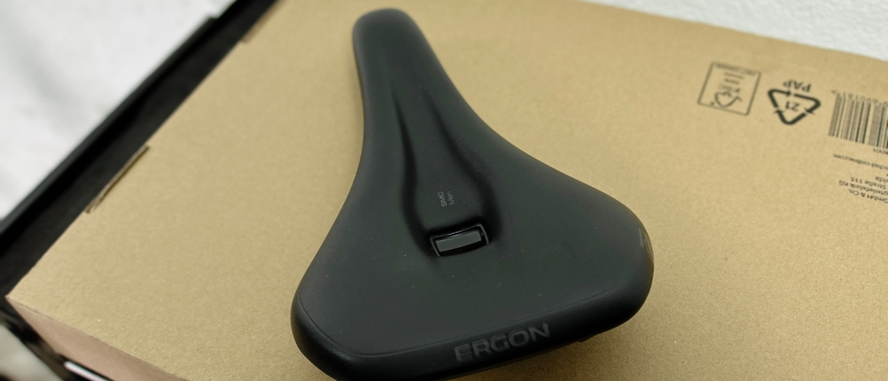 Der Ergon SMC Sport ist von oben fotografiert und liegt auf einem Karton. Sichtbar sind die ergonomische Form und der zentrale Entlastungskanal.