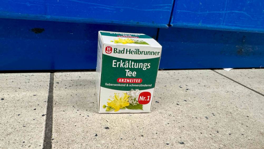 Vor einer blauen Wand steht der getestete Erkältungstee auf dem Boden.
