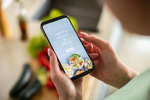 Kalorienzähler-Apps im Test: Eine Person hält ein Smartphone in den Händen und sucht damit nach gesunden Rezepten.