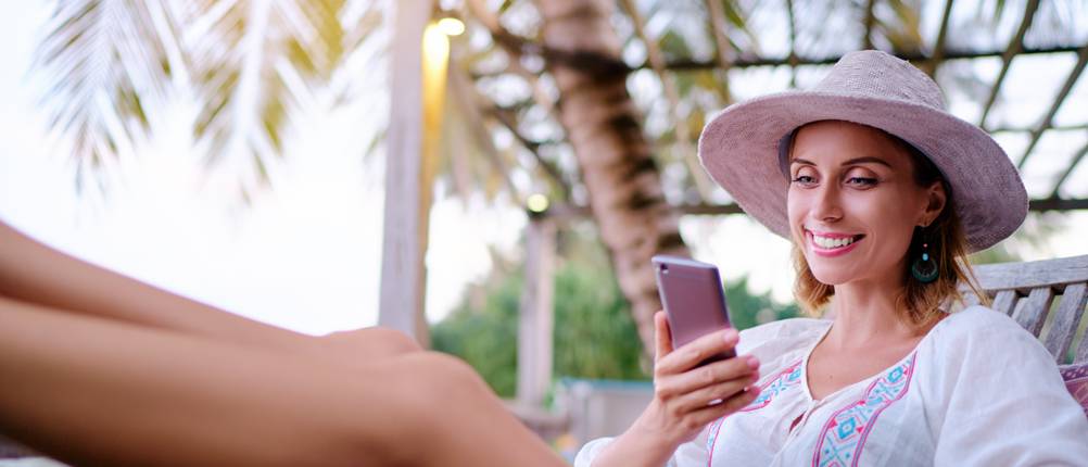 Eine Frau sitzt im Urlaub mit ihrem Smartphone auf einem Stuhl