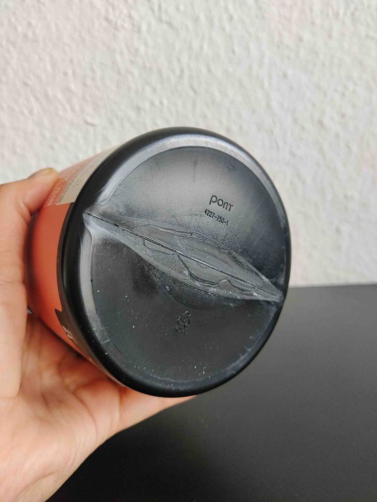 Eine Hand hält den Boden einer Dose des Aminosäure-Komplex vor eine helle Wand.