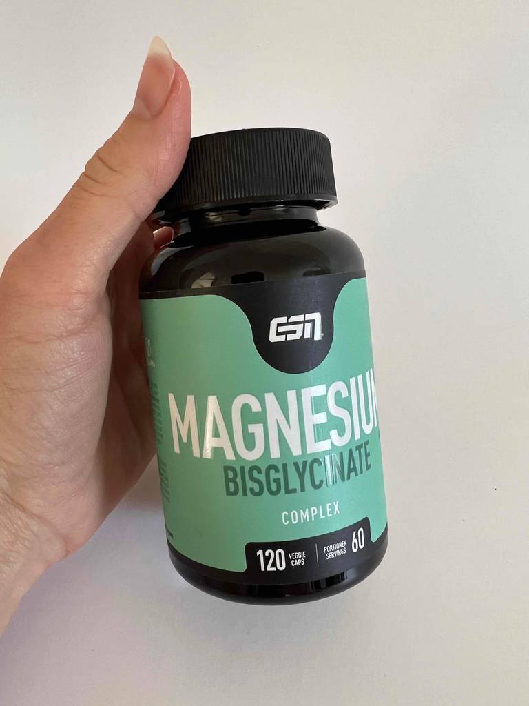 Eine Hand hält einen Drehverschluss-Behälter aus Braunglas mit getestetem, hochdosiertem Magnesium vor weißer Fläche.