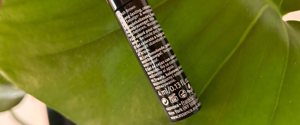 Ein getestetes Augenbrauengel in einer schwarzen Tube inklusive Gebrauchsanwendung vor einem grünen Hintergrund.