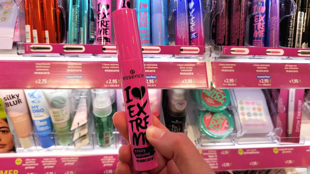 Eine Hand hält den Volumen-Mascara im Testvor einem Regal mit verschiedenen Wimperntuschen.