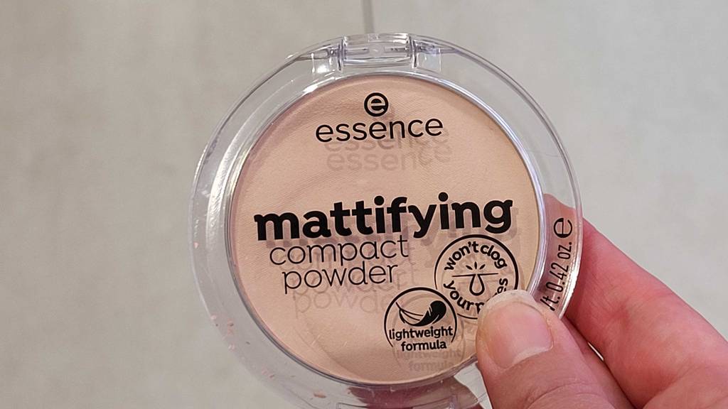 Eine Hand hält eine Dose, mit Sicht auf die vordere Beschriftung eines getesteten Essence Puders vor einem hellen Hintergrund.