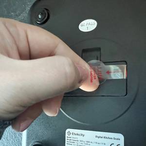 Jemand zieht die Lasche für den Betrieb der Küchenwaage Etekcity Ek6020 ab.