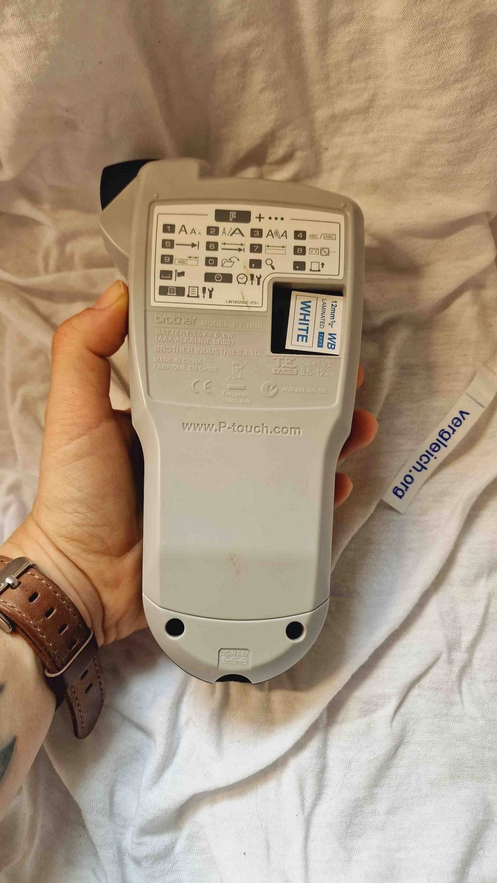 Im Test: Eine Hand hält einen Etikettendrucker mit der Rückseite nach oben vor einen hellen Stoff.