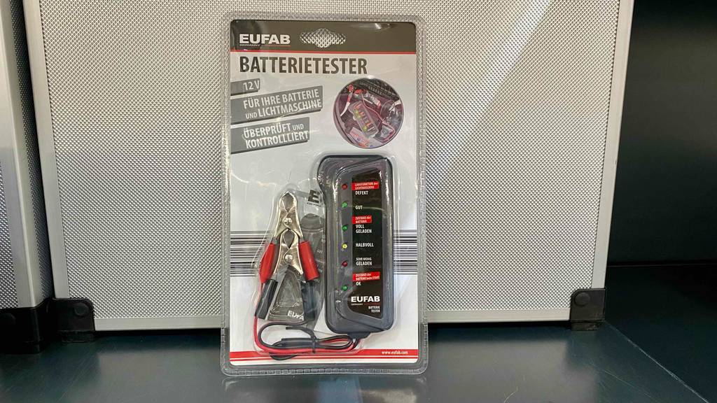 Autobatterietester im Test: Ein 12-Volt-Tester der Marke EUFAB lehnt eingeschweißt in der transparenten Verpackung an einer Metallkiste.
