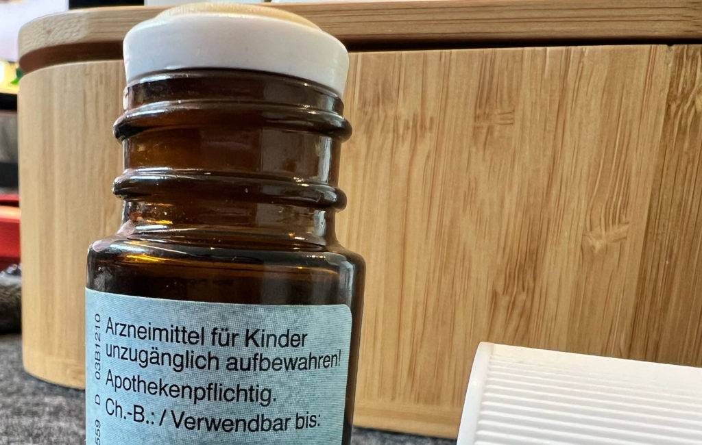 Ein blickdichtes Fläschchen mit getestetem Pfefferminzöl steht geöffnet, mit Fokus auf Arzneimittelhinweis vor einer Holzbank.