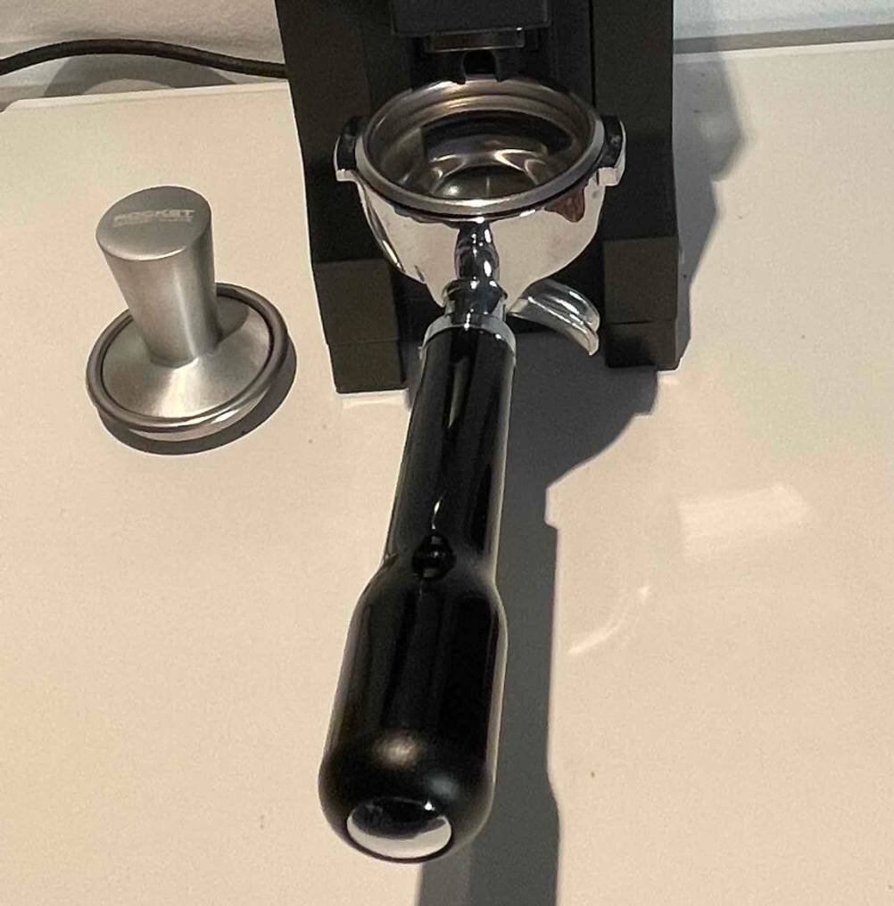 Detailansicht des Siebträgers inklusive Tamper vor einer Siebträger-Kaffeemühle im Test.