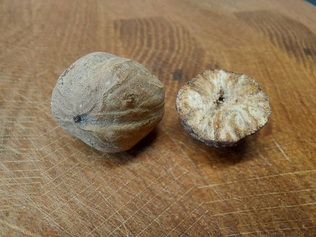 Im Test: eine ganze Muskatnuss liegt neben einer halben auf einer dunklen Holzfläche.
