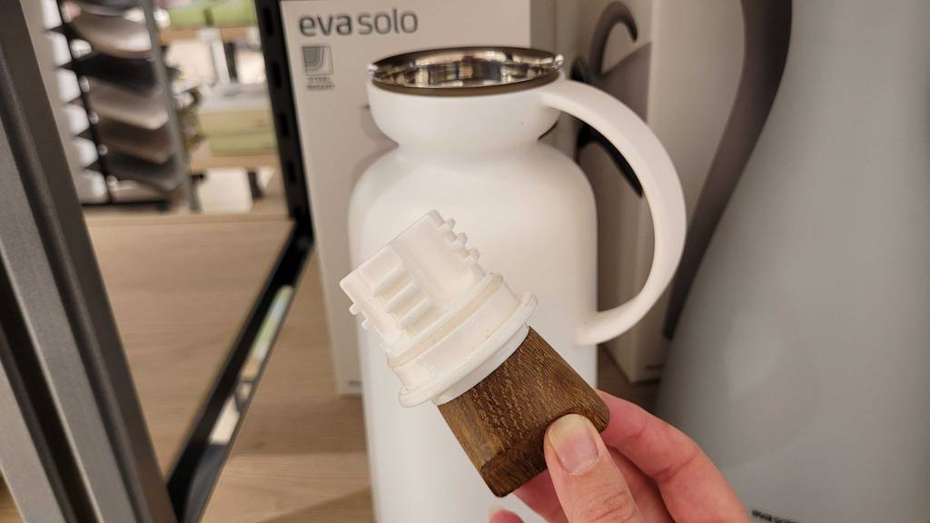 Eine Hand hält den Schraubverschluss vor einer getesteten Thermoskanne.