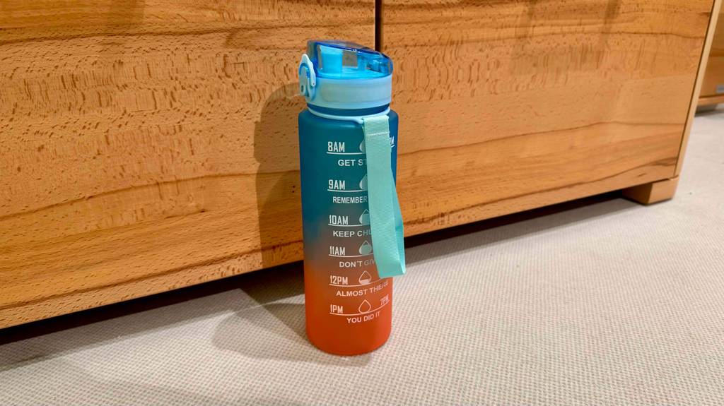Eine blau-orange getestete Fitness-Trinkflasche steht vor einer Holztruhe.