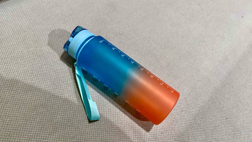 Getestet: Eine Fitness-Trinkflasche in Blau-Orange liegt auf einem hellen Untergrund.
