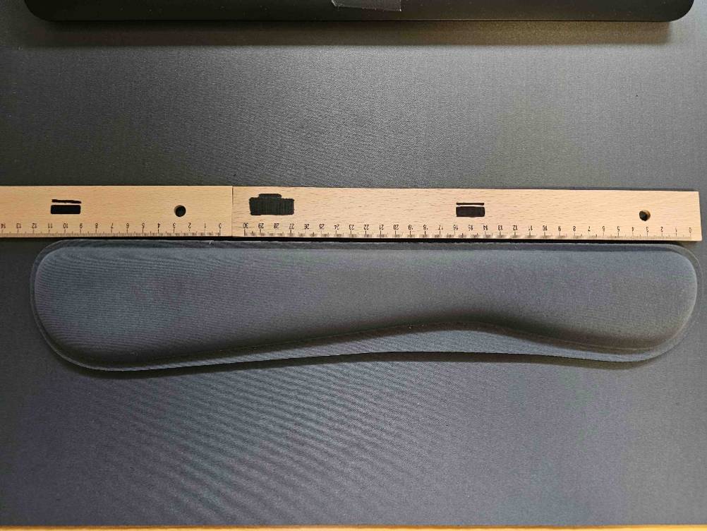 Mit einem Holzlineal, das über einer getesteten Handballenauflage für die Tastatur liegt, wird die Breite gemessen.