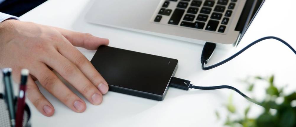 Ein Mann greift nach einer getesteten externen Festplatte neben dem Laptop.