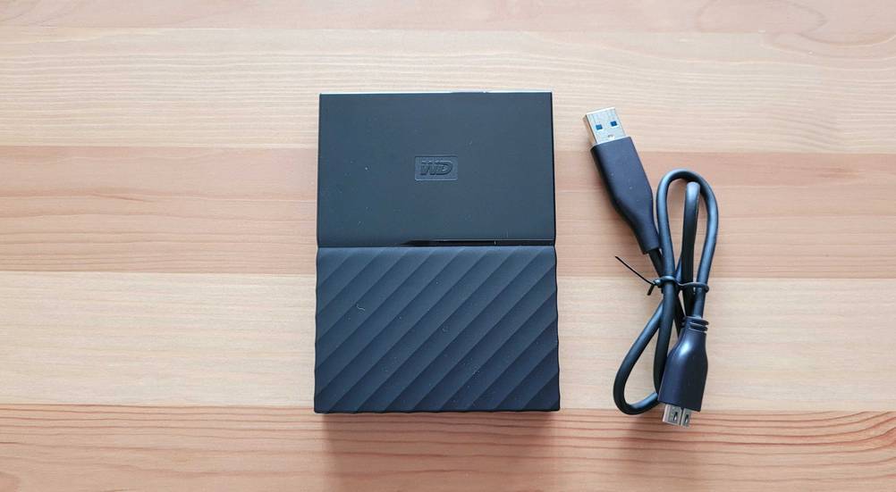 Eine getestete Externe SSD-Festplatte (1TB) neben ihrem Anschlusskabel auf einem Holztisch von oben.