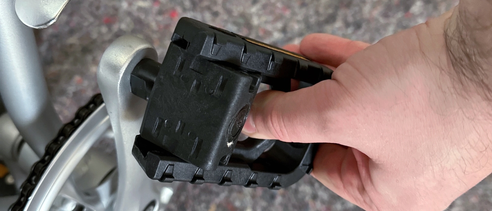 Das Bild zeigt ein montiertes Pedal am FabricBike Folding Space Grey. Eine Hand dreht das Pedal in die Position zur Arretierung oder Demontage.