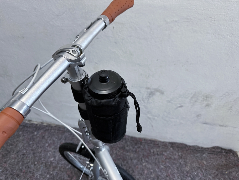Das Bild zeigt den Lenkerbereich des FabricBike Folding Space Grey mit montierter Trinkflaschenhalterung und schwarzer Flasche in einer Haltertasche.
