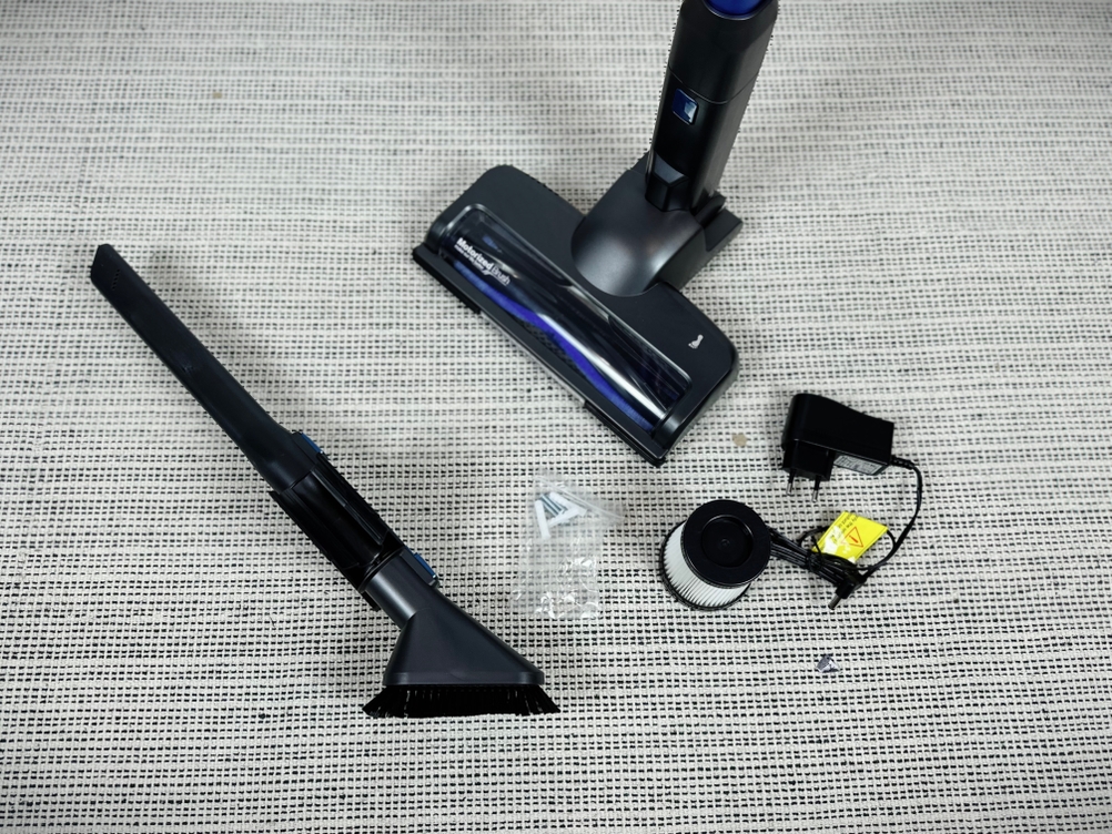 Das Zubehör des Fabuletta FSV001 liegt auf einem hellen Teppich. Zu sehen sind Fugendüse, Bürstenaufsatz, Ladegerät, HEPA-Filter und Bodendüse.