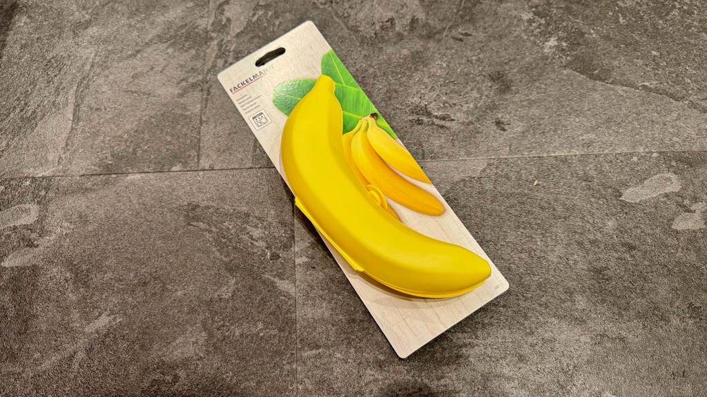 Eine gelbe getestete Bananenbox im Test liegt inklusive Verpackung auf einem Fliesenbelag.